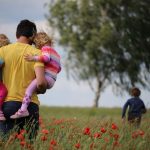 Vater mit 2 kleinen Kinder spaziert durch Wiese mit Mohnblumen