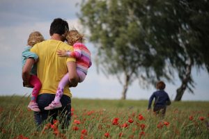 Vater mit 2 kleinen Kinder spaziert durch Wiese mit Mohnblumen